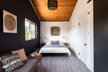 Bold bedroom with gray wood floor, wood ceiling, black-white walls and wicker accents