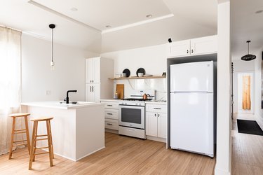 Minimalist kitchen with white walls and cabinets, wood floors, and black accents