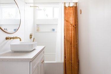 A minimalist white walled bathroom with a white vanity and gold-orange accents