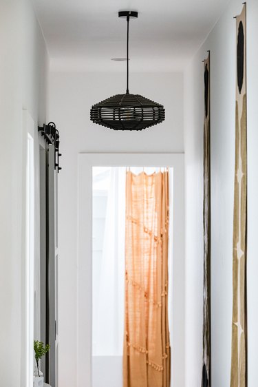 Hallway Lighting Ideas with A black abstract pendant light in a white-walled hallway and an orange curtain