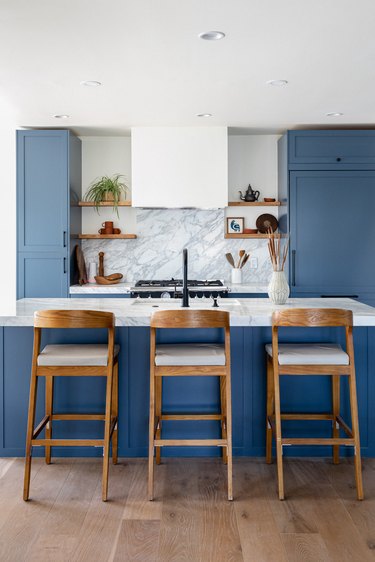 Should Wall Color Match Kitchen Cabinets in A kitchen with blue cabinets and wood bar stools at a kitchen island