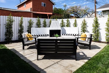 A backyard with a white fence and white furniture on top of a concrete paver patio