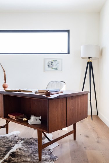 A wood desk on wood floor with a fur rug and a black-white floor lamp