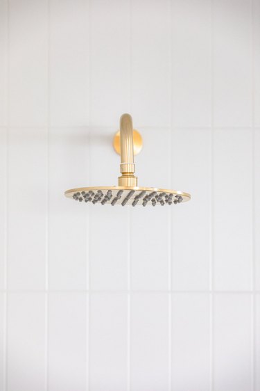 A gold shower head and a white tile wall