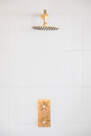 eco-friendly bathroom idea with gold showerhead and white tile wall