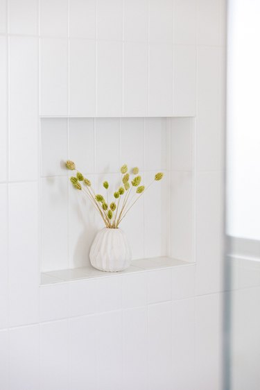 A white wall niche with a vase of plant clippings