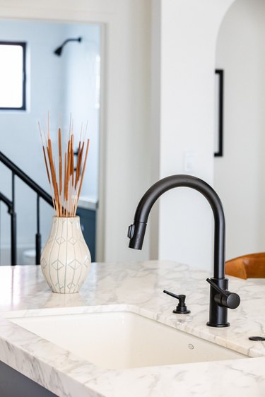 White kitchen sink countertop with a black faucet and a white vase with dried plants
