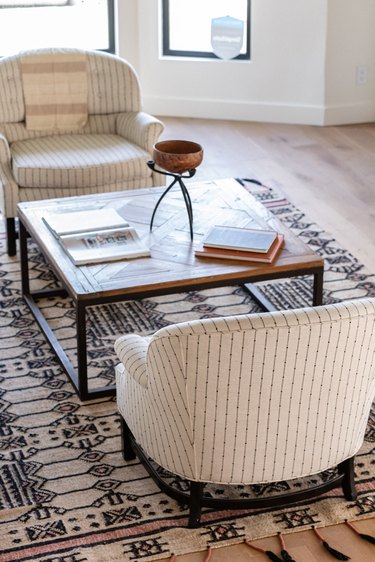 Beige living room chairs with a wood coffee table, beige-black rug and wood floors