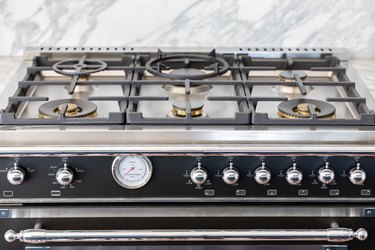 A stove top with a gray-white granite backsplash