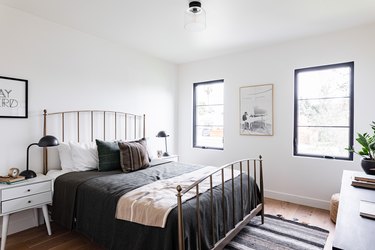 A bedroom with an iron bed rail, a rug, and a white dresser