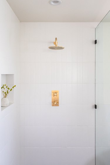 shower with white ceramic tile, glass panel, and gold shower faucet and showerhead