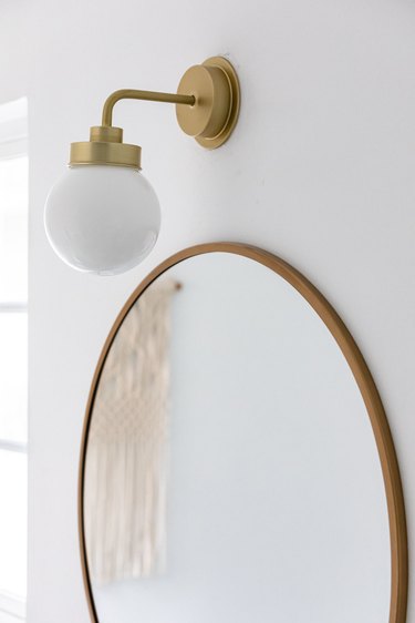 A large round bathroom mirror with a globe light fixture