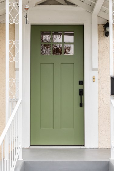 A green entrance door with gray steps and a white banister