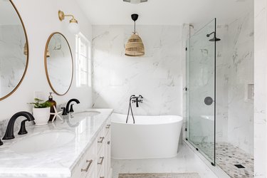 Minimalist white bathroom with a glass shower, bathtub, and large round mirrors