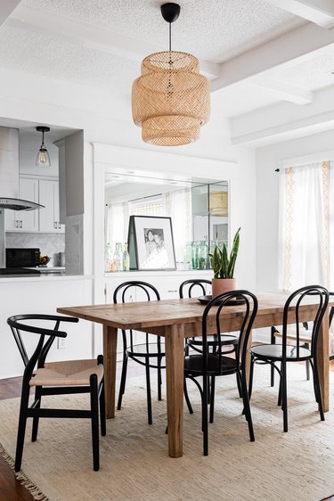 Wood dining table with black chairs on a neutral fiber rug and a wicker pendant light