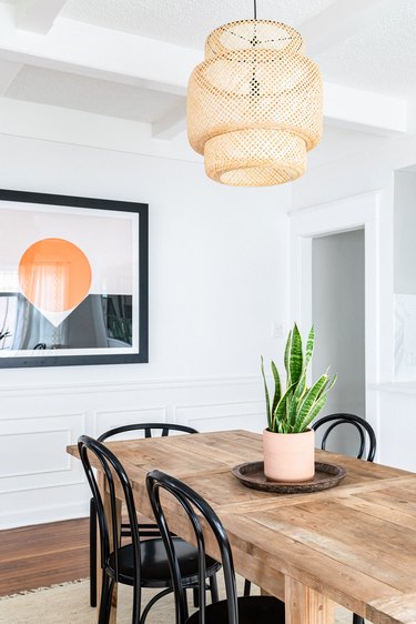 Dining room with a wood dining table, snake plant, wicker pendant light and art