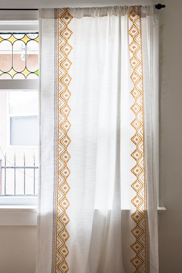 A stained glass window with yellow embroidered white curtains