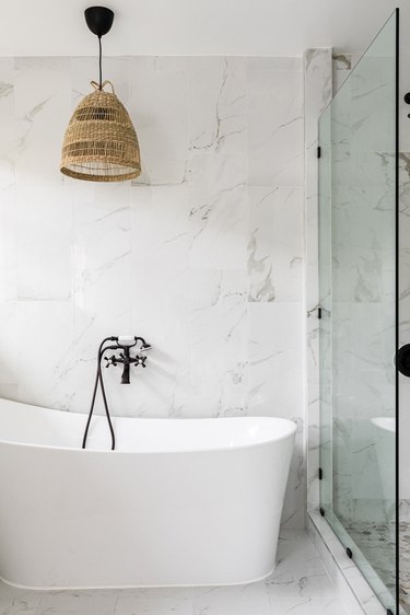 A stunning blue bathroom with a freestanding bathtub, walk-in shower, and  double sinks. The bathtub is positioned in the center of the room, with a  large window behind it that lets in