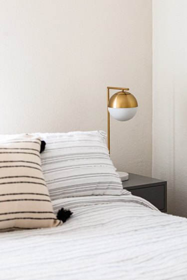 A globe table lamp on a nightstand and a bed with striped bedding and pillows