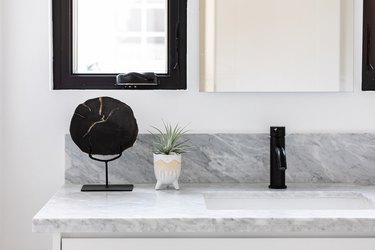 Marble countertop for sink in bathroom with mirror and small plant, with mirror and small cabinet on white wall