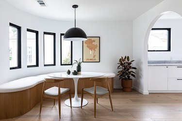 Contemporary curved dining room with curved bench, small round table, chairs, pendant lamp, and tall windows with view of hallway via archway