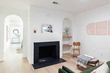 Contemporary living room with black fireplace, alcove with plants, green couch, hexagonal ottoman, and archway leading to hallway