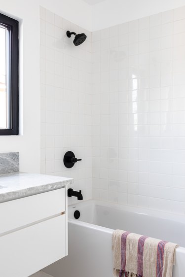 Modern bathroom with white bathtub with black faucet, white and purple towel hanging on the tub, and marble countertop