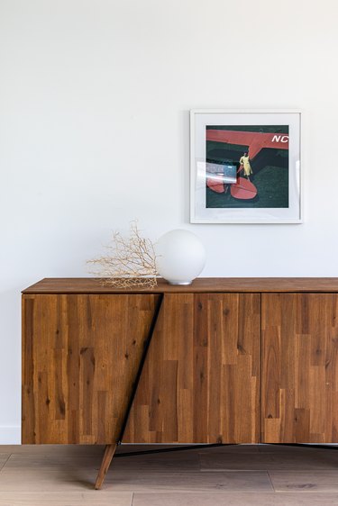 hallway lamp idea with Wood paneled cabinet with globe light against white wall with small hung painting on hardwood floor