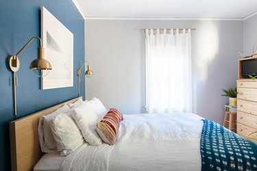 Золотой одиночный карниз для штор, на котором висят прозрачные шторы в голубой спальне