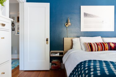 Bedroom with bright blue walls, gold sconce and a white door.