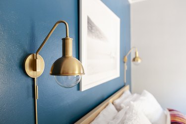 Blue bedroom wall with double gold globe sconces and framed artwork over a bed.