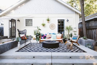 Patio with a black and white zig-zag rug, eclectic Modernist chairs, plants, and a fire pit.