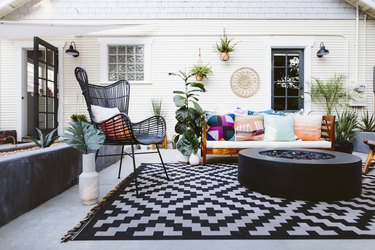 A colorful patio with modern seat and a black gas fire pit over a black and white rug