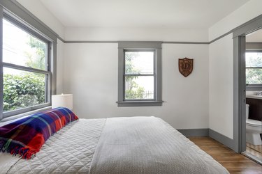 Minimalist bedroom with gray bedding, plaid pillows, wood floors and gray framed windows