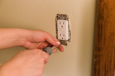 Person using a screwdriver to screw in place GFCI outlet