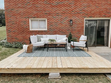 Wood platform deck with a blue diamond rug, wood slat coffee table, and white cushioned seating