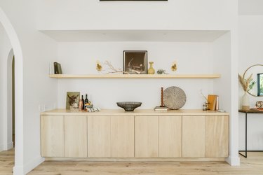 Large wall niche with a light wood sideboard and shelf with art and accent pottery