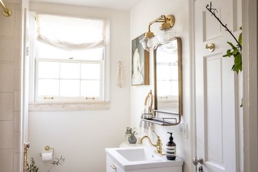 Minimalist white bathroom with a white vanity, gold faucet sink and a multi-sconce