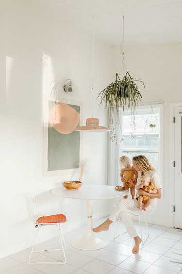 Woman in white kitchen sitting at white tulip table holding her baby