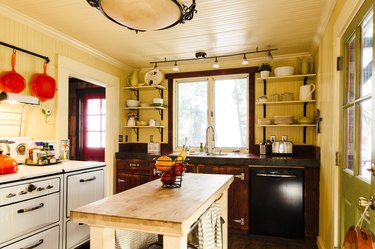 A bight, yellow-walled kitchen with retro cabinets and stove and wood kitchen island