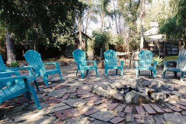 A backyard with light blue Adirondack chairs on a slate patio with a fire pit