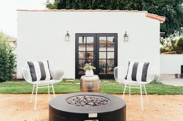 California-modern style backyard space with black fire pit, two white chairs, black and white pillows, and a metallic side table.