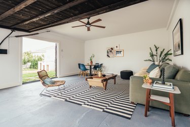 Small Garage Ideas in a Living room in a California-bohemian style: cement floor, wood ceiling, ceiling fan, black and white rug, rattan accent chair, plant, coffee table and couch.A renovated garage with living area, cement floor, and wood ceiling.