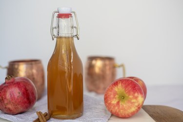 Glass bottle with a cinnamon simple syrup, on a table with apples and copper mule mugs