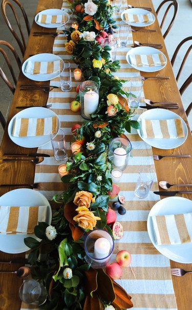 A long thanksgiving table with a white and gold striped runner and matching napkins on each plate