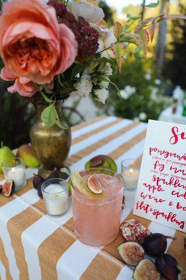 a table laden with fruit, flowers, a cocktail, and a hand-written menu