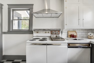 Retro minimalist kitchen with white cabinets, mid-century oven, gray window frames, and checkered floor
