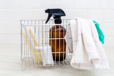 wire white basket filled with amber spray bottle, brush, sponge, and rags