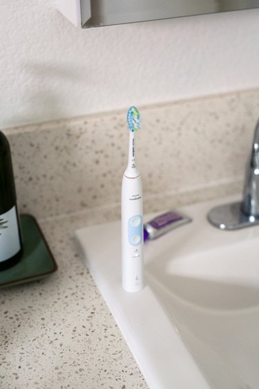 An electric toothbrush and tube of toothpaste on a sink