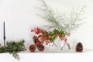 fresh red flowers in clear glass vases on mantel with pinecones and winter greenery